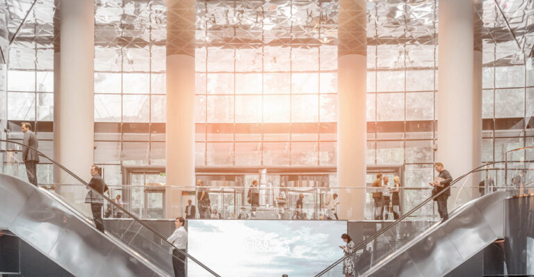 glass building in sunset with people going up and down the escalator